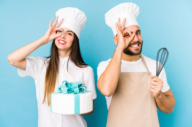 Jong stel dat samen een cake kookt geïsoleerd opgewonden houdend ok gebaar op oog.