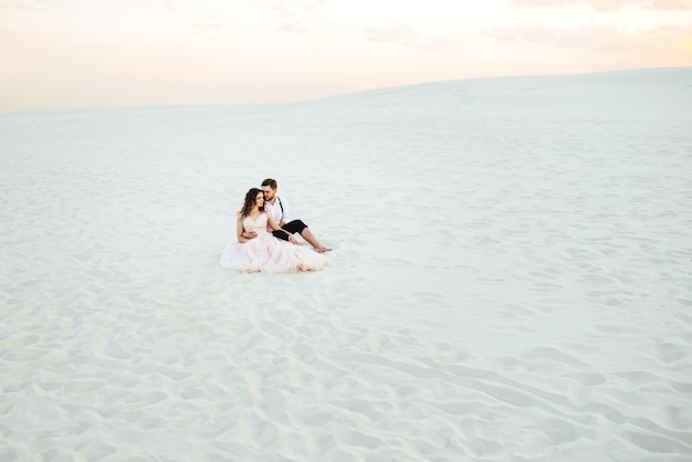 Jong stel een man in zwarte broek en een meisje in een roze jurk lopen langs het witte zand van de woestijn