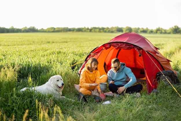 Jong stel gaat picknicken met een hond bij de tent op greenfield