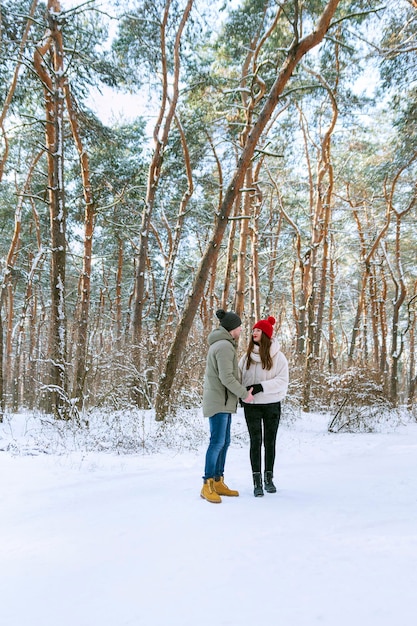 Jong stel geliefden staat in het winterbos en kijkt elkaar aan. Mensen buitenshuis. Verticaal kader.