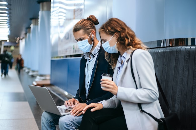 jong stel in beschermende maskers met behulp van een laptop op het metro-platform