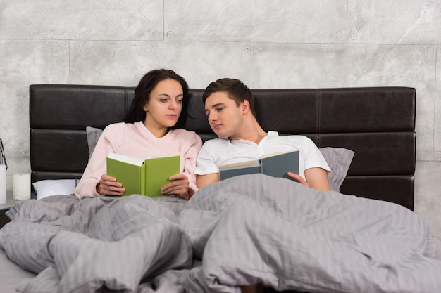 Jong stel leest elkaar boeken terwijl ze in bed liggen en een pyjama dragen in de slaapkamer in loftstijl met grijze kleuren