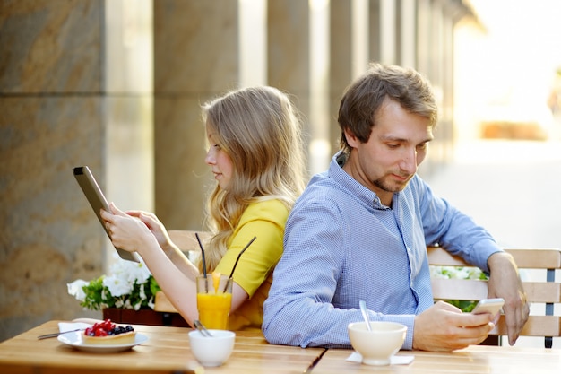 Jong stel met behulp van slimme telefoon en tablet pc in het buitencafé