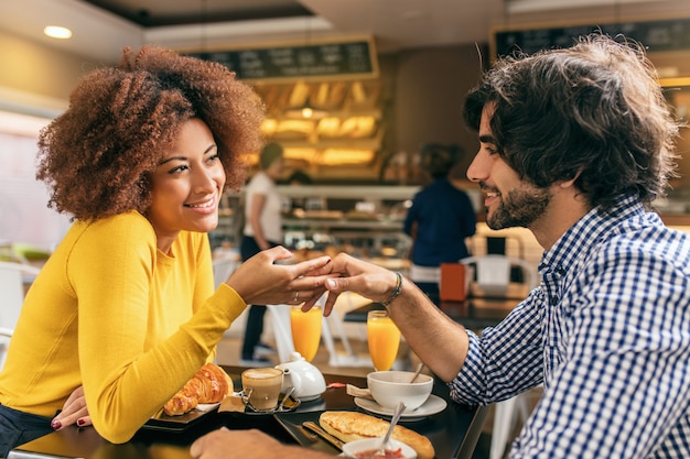 Jong stel met een ontbijt in het café, hun hand strelend, ze zijn verliefd