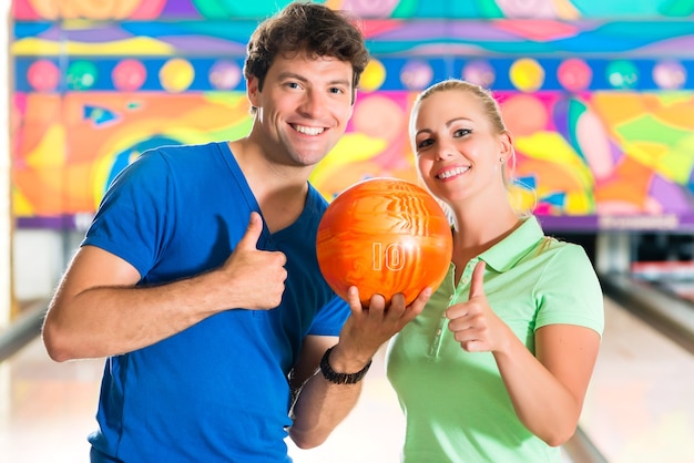 Jong stel of vrienden, man en vrouw, bowlen met een bal voor de tien-pin alley, ze zijn een team