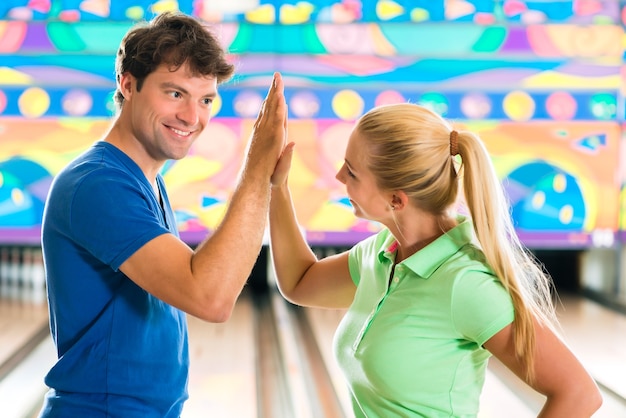 Jong stel of vrienden, man en vrouw, spelen bowling voor de kegelbaan, ze zijn een team