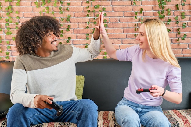 Jong stel van een Afro-Amerikaanse jongen en een blond meisje die high fives van videogames spelen