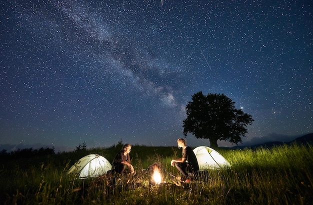 Jong stel zit bij verlichte tenten in de buurt van kampvuur