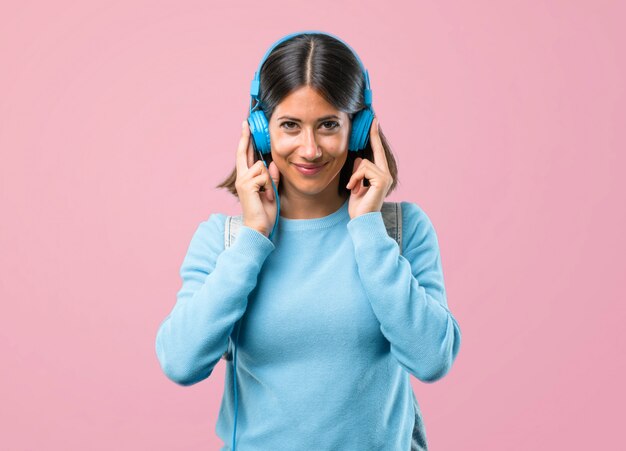 Jong studentenmeisje met blauwe sweater het luisteren muziek op roze achtergrond.