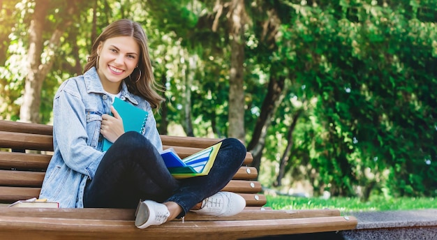Jong studentenmeisje zit op een bankje in het park en houdt boekennotitieboekjes vast Meisje geeft lessen in het park