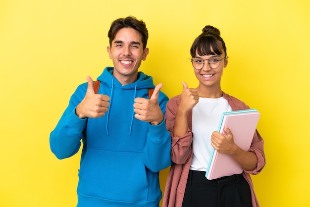 Jong studentenpaar dat op gele achtergrond een duim omhoog gebaar met beide handen geeft en glimlacht