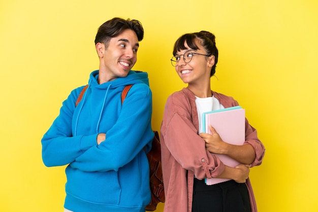 Jong studentenpaar geïsoleerd op een gele achtergrond die met een glimlach over de schouder kijkt