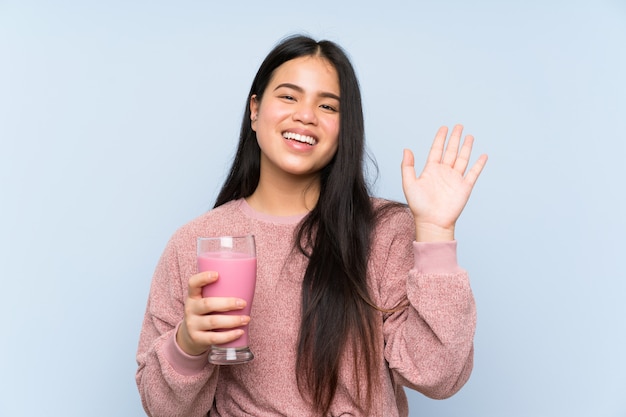 Jong tiener Aziatisch meisje met aardbeimilkshake het groeten met hand met gelukkige uitdrukking