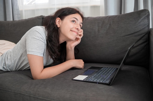 Jong tienermeisje chatten met vrienden online op laptop liggend op de bank