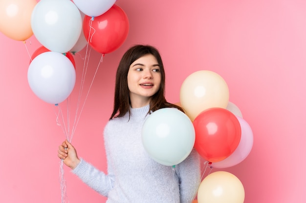 Jong tienermeisje dat veel ballons over roze muur houdt