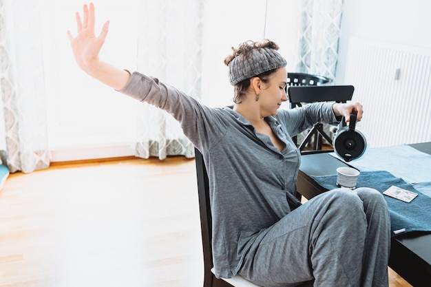 Jong tienermeisje, in pyjama, haarband, zit op een stoel in de eetkamer, drinkt koffie in de ochtend