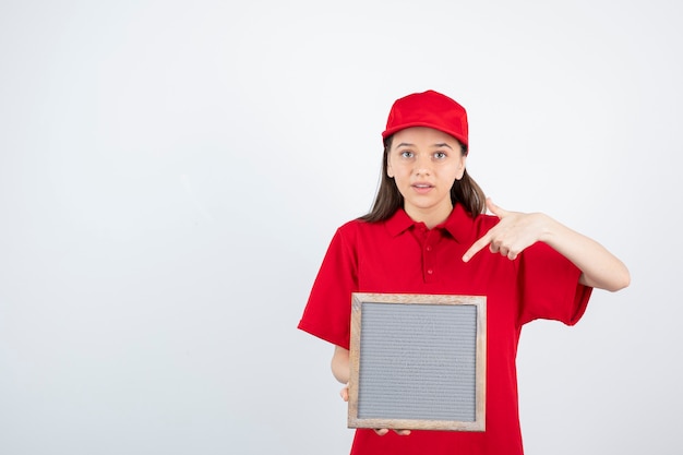 jong tienermeisje in rood uniform permanent en wijzend op frame