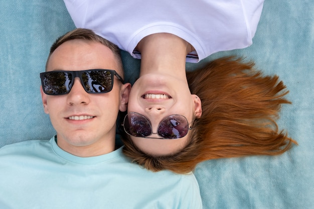 Jong tienerpaar die in zonnebril samen op blauwe doek leggen die liefde van relaties genieten.