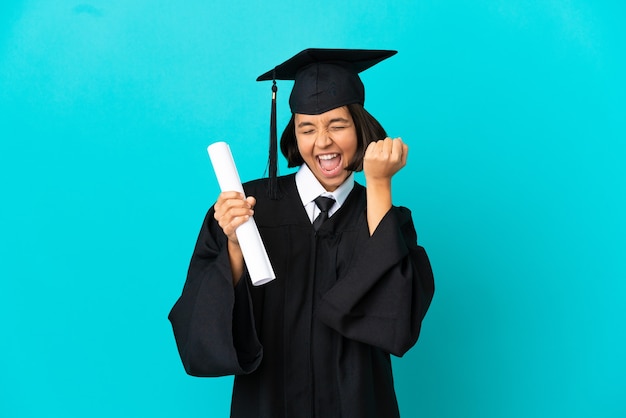 Jong universitair gediplomeerd meisje over geïsoleerde blauwe achtergrond die een overwinning viert