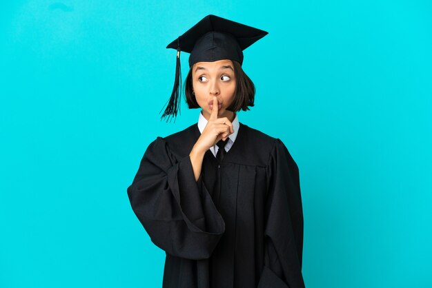 Jong universitair gediplomeerd meisje over geïsoleerde blauwe achtergrond die een teken van stiltegebaar toont dat vinger in mond stopt