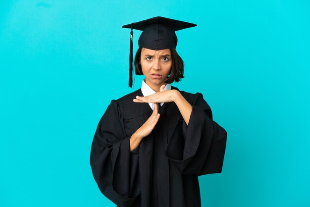 Jong universitair gediplomeerd meisje over geïsoleerde blauwe achtergrond die een time-outgebaar maakt