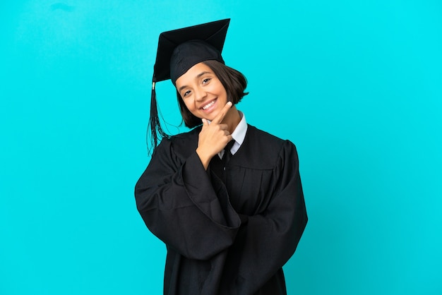 Jong universitair gediplomeerd meisje over geïsoleerde blauwe achtergrond gelukkig en glimlachend