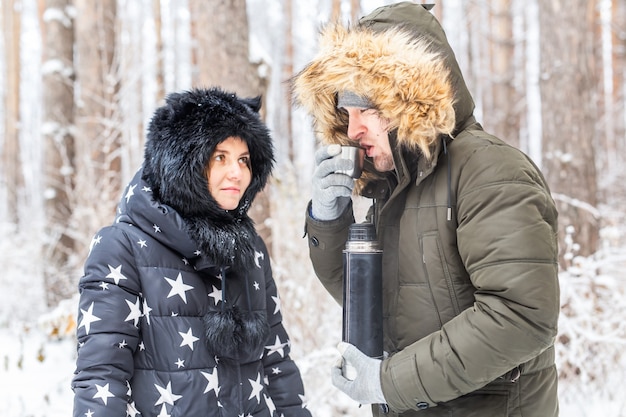 Jong verliefd stel drinkt een warm drankje uit een thermoskan en geniet van de winterse natuur