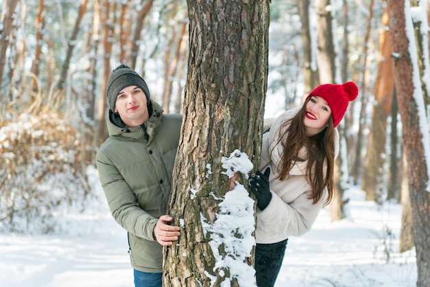 Jong verliefd stel gluurt achter een boom in het besneeuwde bos Liefdesverhaal fotoshoot