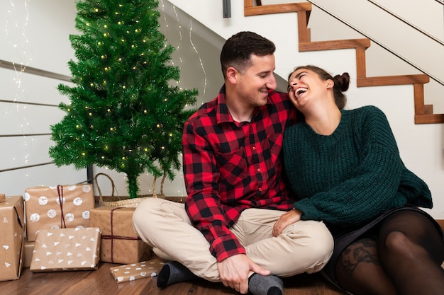 Jong verliefd stel lachen samen in de buurt van de kerstboom en een stapel geschenken Vakantieconcept