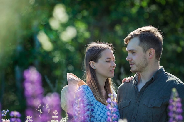 Jong verliefd stel lacht en knuffelt in de natuur in bloemen prachtig park met bloeiende paarse lupines liefde en tederheid