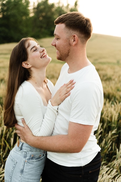 Jong verliefd stel staat in een tarweveld bij zonsondergang van de dag. man met een meisje op een romantische zomerdate. schattig paar geliefden