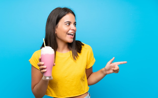 Jong verrast meisje met aardbeimilkshake en wijzende vinger aan de kant