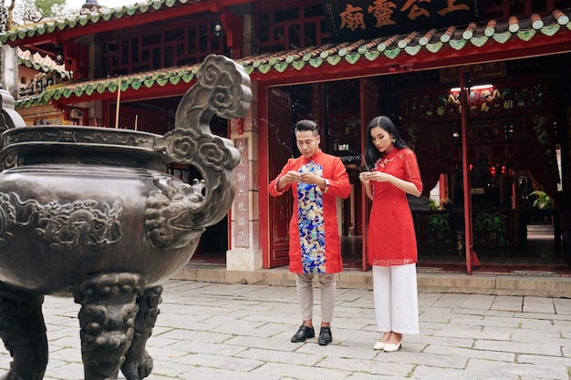 Jong vietnamees koppel in traditionele kostuums bidden met rokende stokken in handen in de boeddhistische tempel