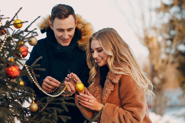 Jong volwassen koppel siert kerstboom in winter forest. Nieuwjaar pine vakantie feest viering concept.