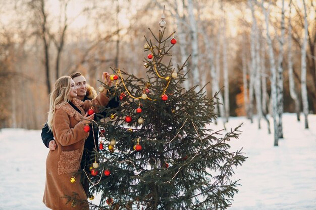 Jong volwassen koppel versiert kerstboom in winterbos Nieuwjaar pine vakantie feest viering concept