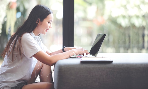 Jong vrij Aziatisch meisje dat vrijetijdskleding draagt die met laptop werkt