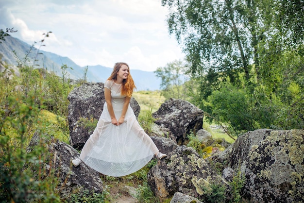 Jong vrolijk meisje in witte jurk poseren op berg achtergrond op zomerdag. Brunette plezier in de natuur. Ruimte kopiëren.