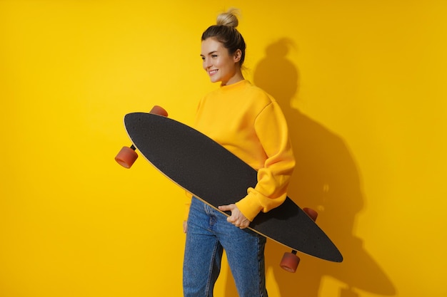 Jong vrolijk meisje met longboard tegen gele achtergrond
