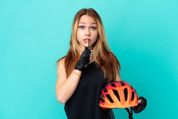 Jong wielrennermeisje over geïsoleerde blauwe achtergrond die een teken van stiltegebaar toont dat vinger in mond stopt