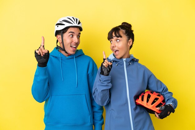 Jong wielrennerspaar geïsoleerd op gele achtergrond met de bedoeling de oplossing te realiseren terwijl ze een vinger optillen