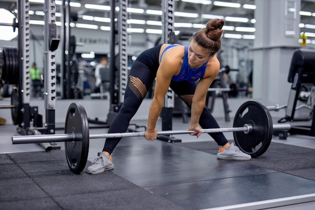 Jong wijfje dat op zwaar werk berekende hurkzit in gymnastiek met barbell doet vrouw met perfecte buikspieren