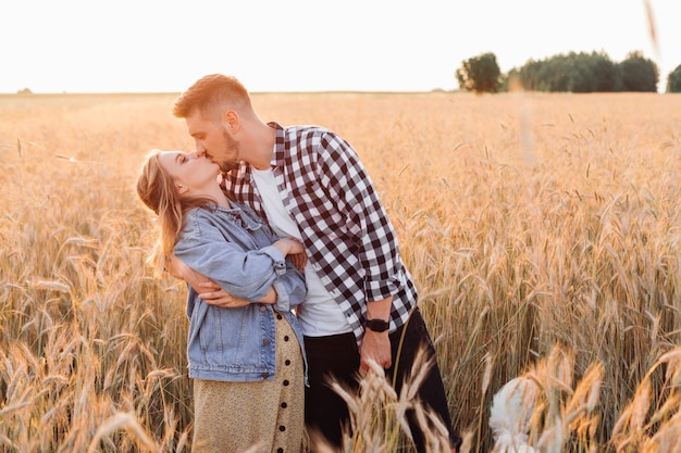 Jong zwanger koppel zoent in het veld tijdens avondwandeling op zomeravond. Zwangerschap en verzorging. Geluk en tederheid. Zorg en aandacht. Liefde en hoop .Familiewaarden.Een gezonde levensstijl.