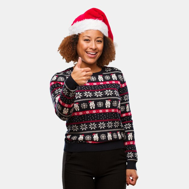 Jong zwarte in een trendy Kerstmissweater met druk die en duim omhoog glimlachen opheffen