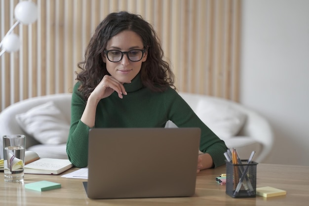 Jonge, aangename Italiaanse vrouw freelancer die op afstand thuis op laptopcomputer werkt