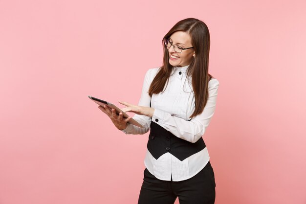 Jonge aangename mooie brunette zakenvrouw houden en gebruiken van tablet pc-computer geïsoleerd op pastel roze achtergrond. dame baas. prestatie carrière rijkdom concept. kopieer ruimte voor advertentie.