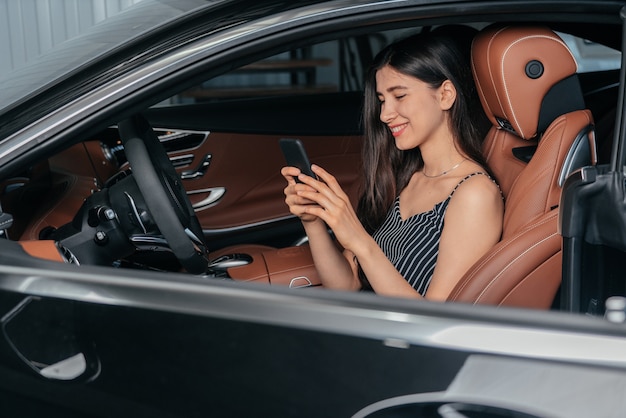 Jonge aantrekkelijke aziatische vrouw die telefoon gebruikt terwijl ze in een luxe auto aan zee zit