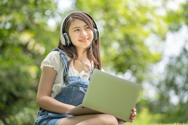 Jonge aantrekkelijke aziatische vrouwelijke werknemer draagt een koptelefoon, luister naar digitale online cursusontwikkelingsstudie online in het park