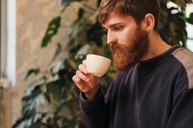 Jonge aantrekkelijke bebaarde man die koffie drinkt terwijl hij alleen in café rust