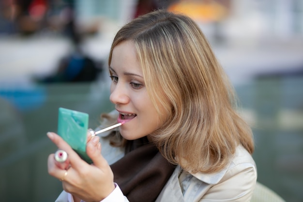 jonge aantrekkelijke blanke vrouw rouge haar lippen met lipgloss en een poederdoos