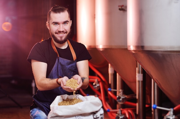 Jonge aantrekkelijke brouwer geniet van het aroma van mout op de achtergrond van de brouwerij en biertanks